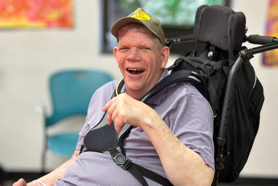 An adult with disabilities smiles at the camera