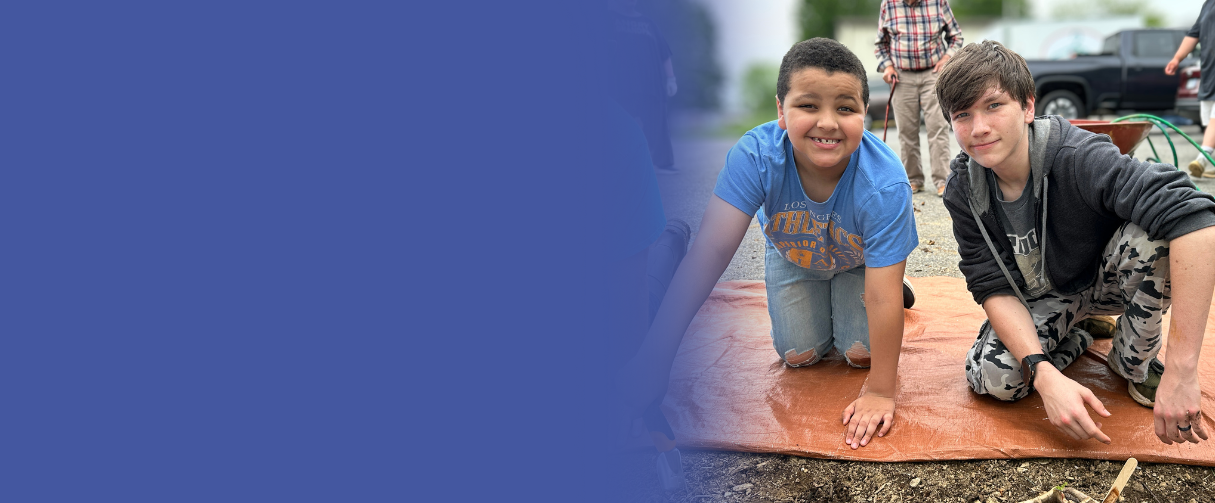 Two students smile at the camera while they garden