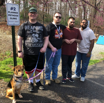Four teenagers stand outside with a dog on a leash who is sitting nicely