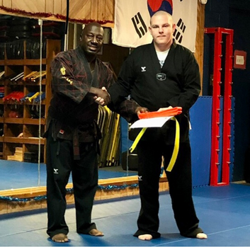 An African American man shakes the hand of a white man in a Taekwondo studio