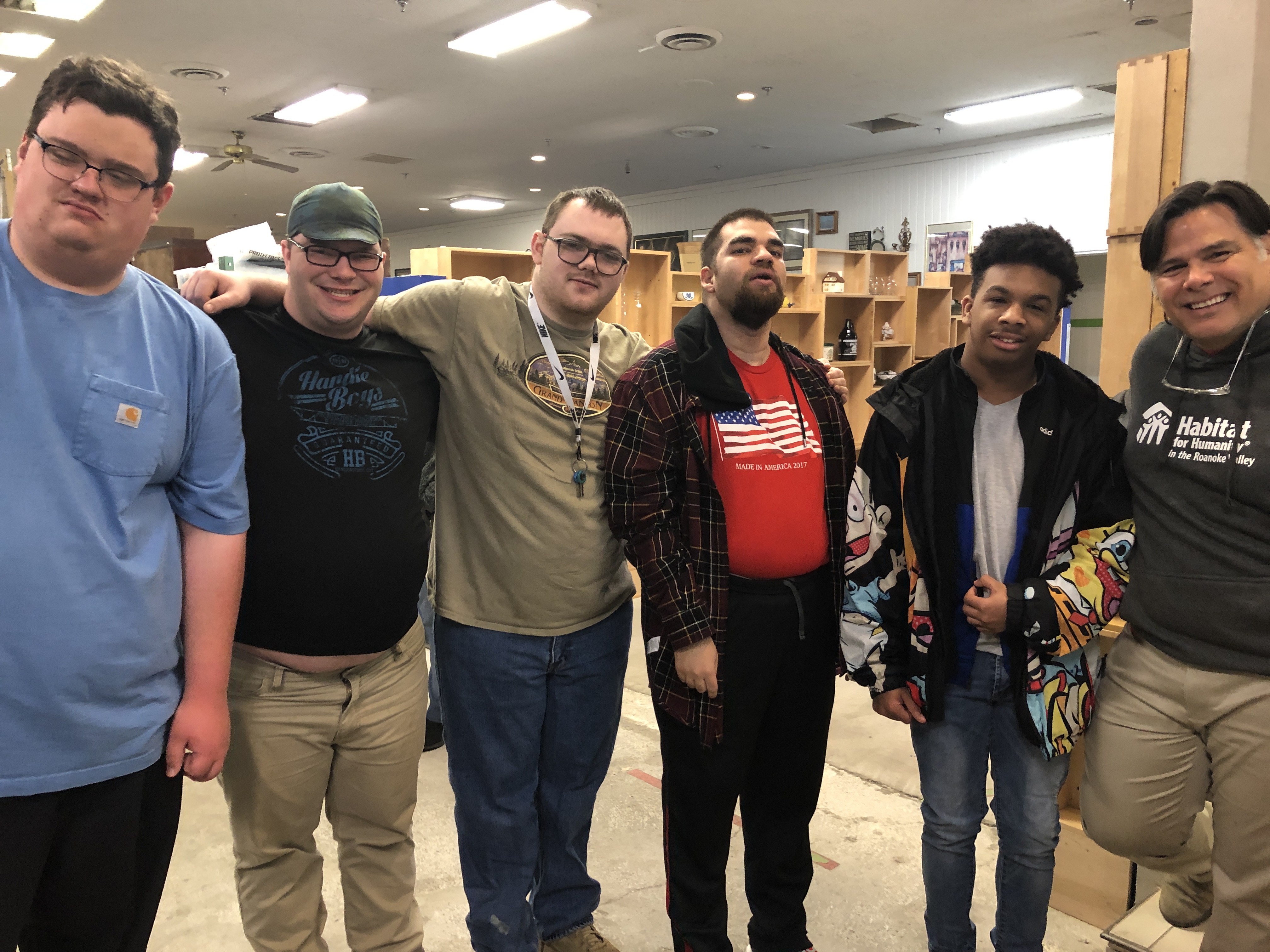 A group of teenagers stands together, smiling, with their arms around each other