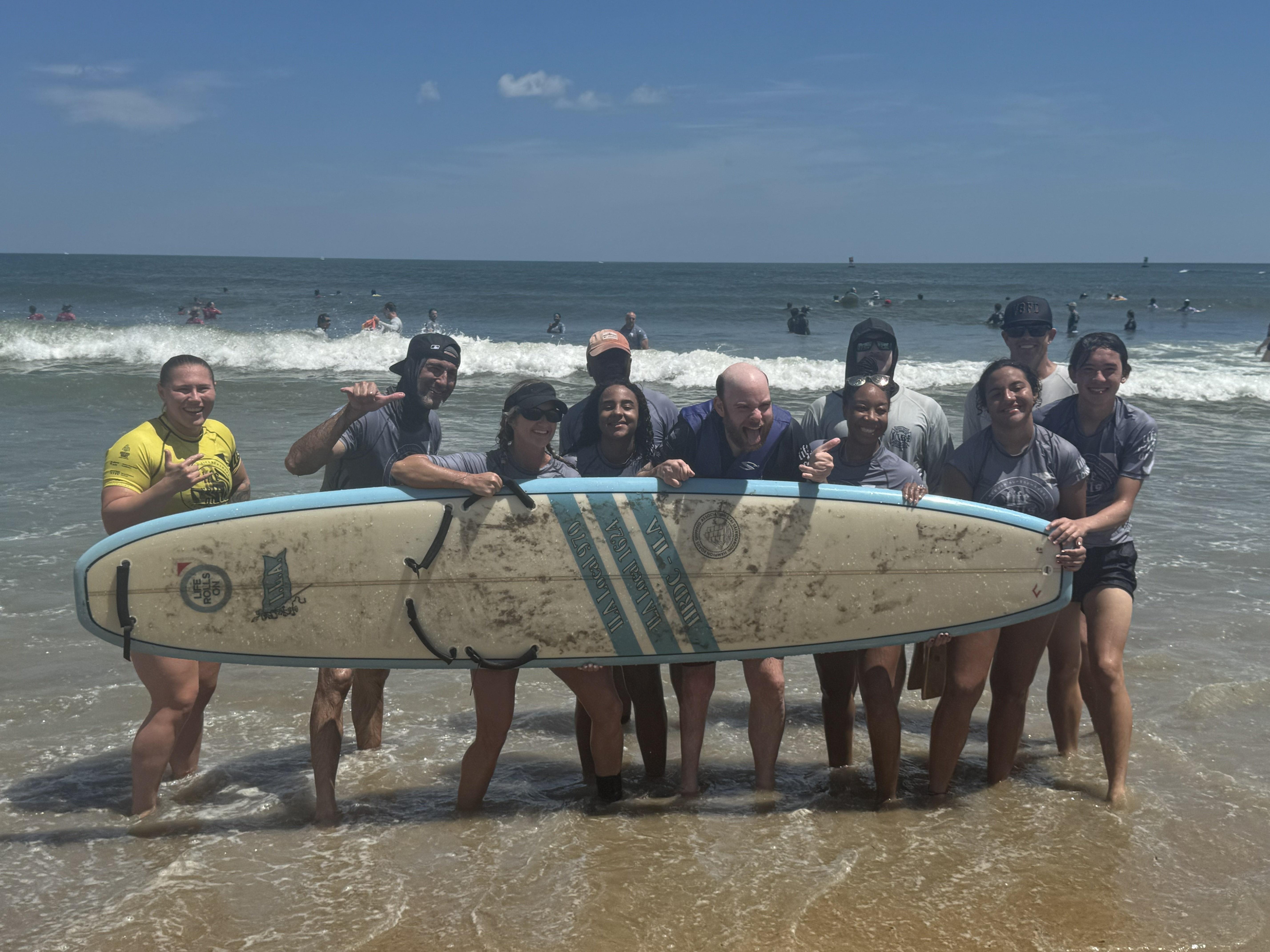 Johnny poses with a group with a surfing board on the beach