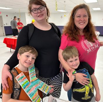 A family stands together in a school cafeteria and smiles at the camera