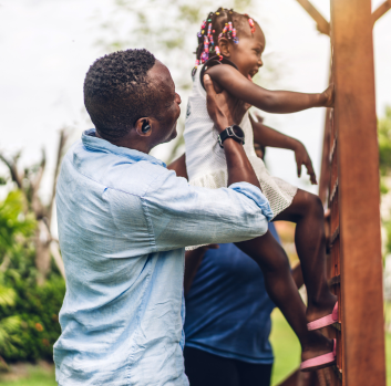 A father helps his daughter climb a play structure