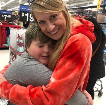 A boy in a great shirt hugs a woman in a red hoodie