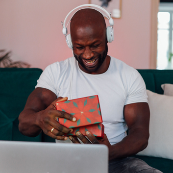 A man smiles while taking the lid off of a gift box during a video chat