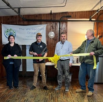 Logan holds giant scissors and cuts a yellow ribbon