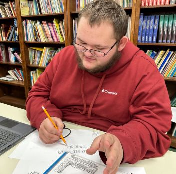 Robert Woody wears a burnt orange sweatshirt and works on an illustration with apencil