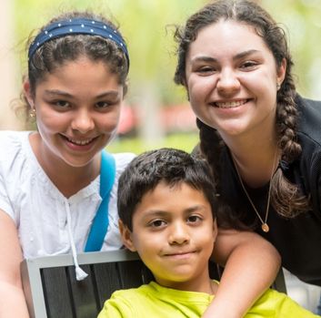 Two Latina or Hispanic tween girls smile over the shoulder of a Latino or Hispanic young boy