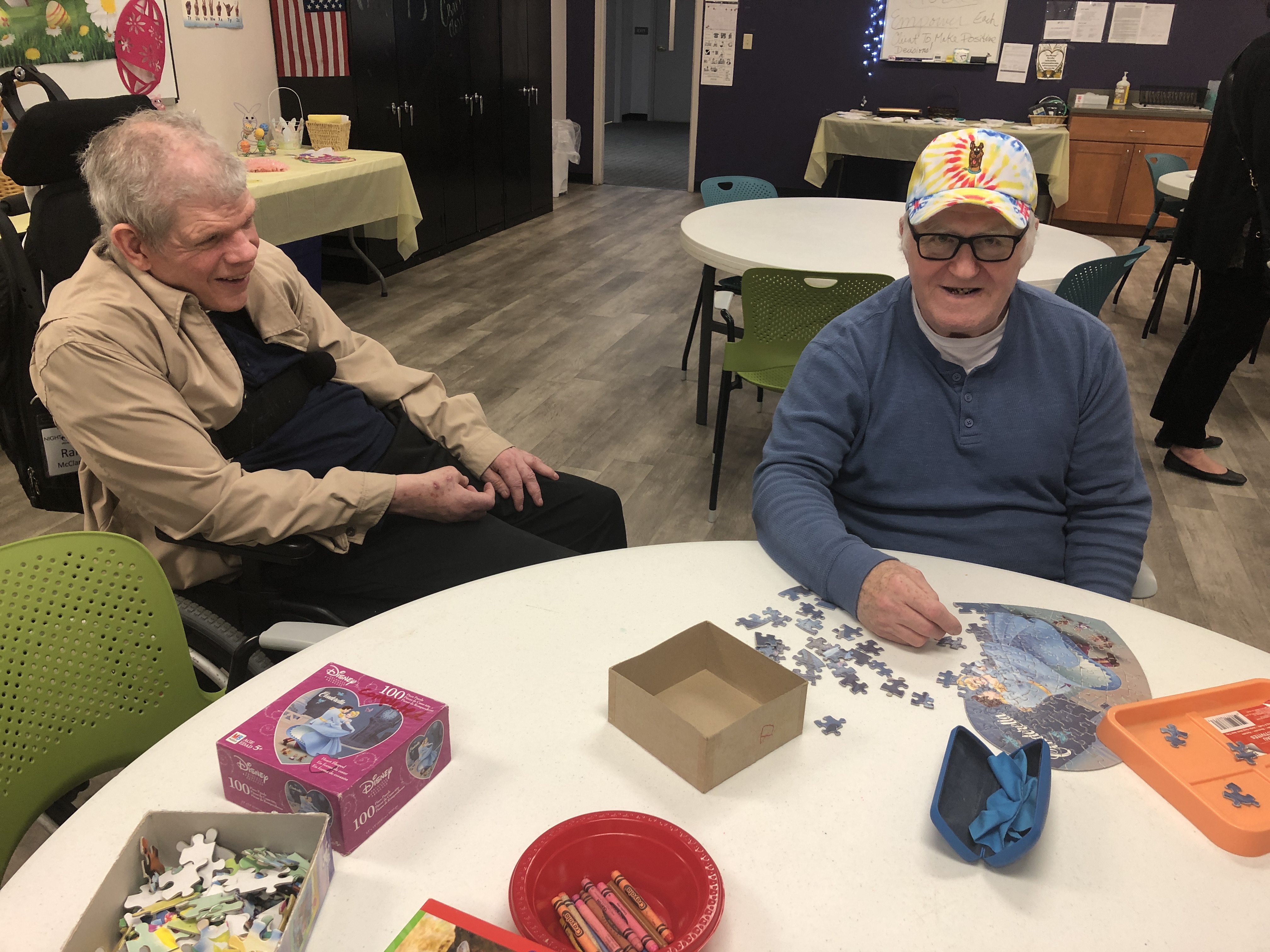 Two elderly men smile and do jigsaw puzzles at a round, white table