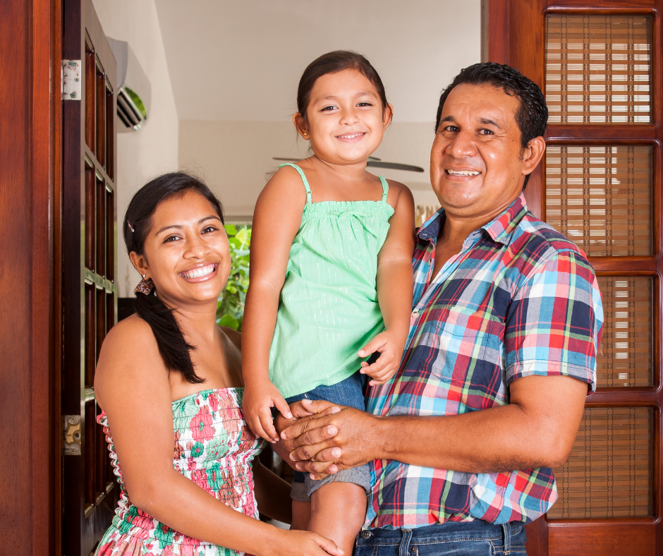 A Latino man and woman hold a school-aged child and smile at the camera