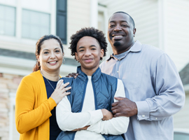 A man and woman smile with a teenage boy in front of a house