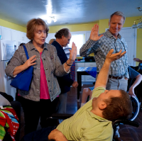 A man in a wheel chair high fives another woman and man