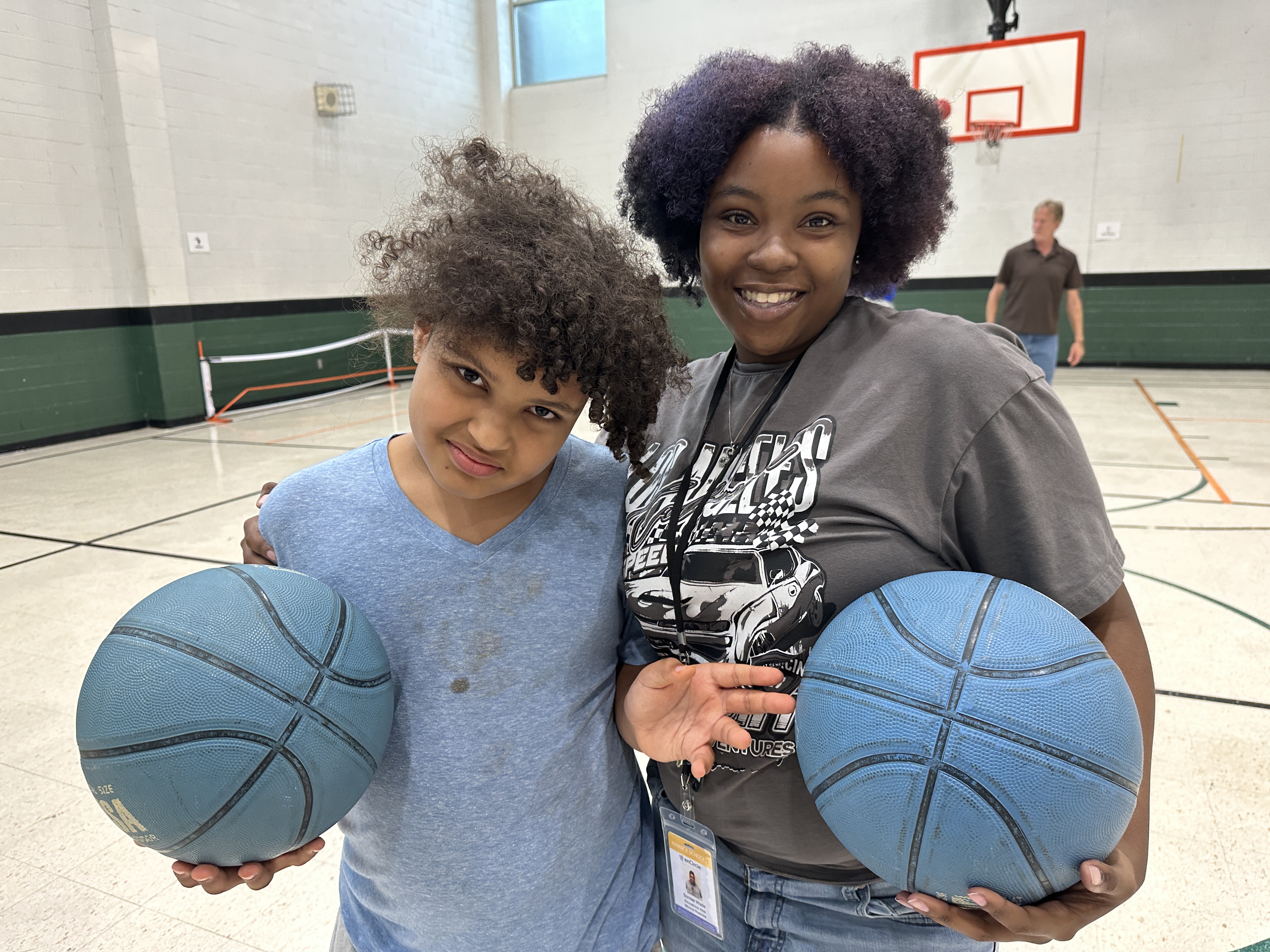 A student and teacher holding basketballs in a gym smile at the camera together