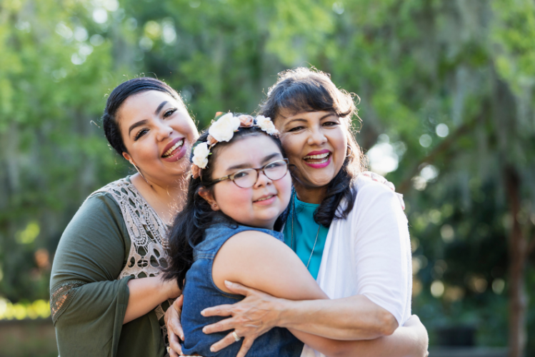 A woman hugs a younger girl while another family member stands by them