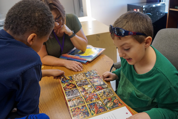 Two students and a teacher look at a book together