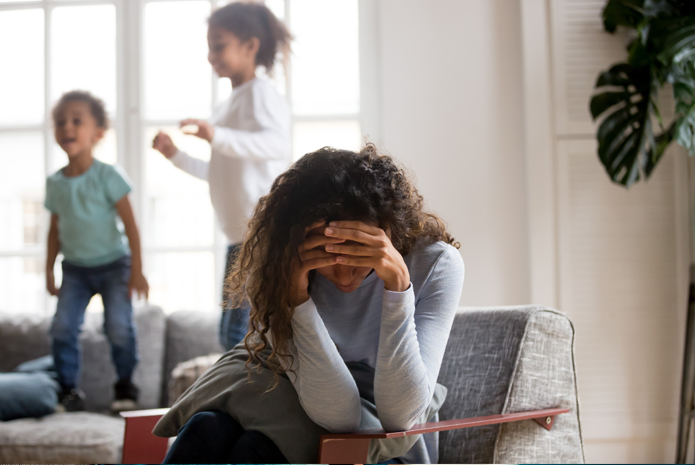 A woman hangs her head in grief as two children play behind her