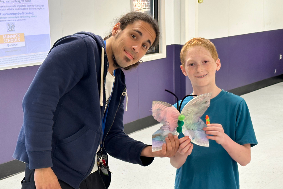 A smiling boy holds a craft butterfly he made while a school administrator smiles next to him